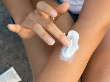 A close up of a hand applying cream on an arm.
